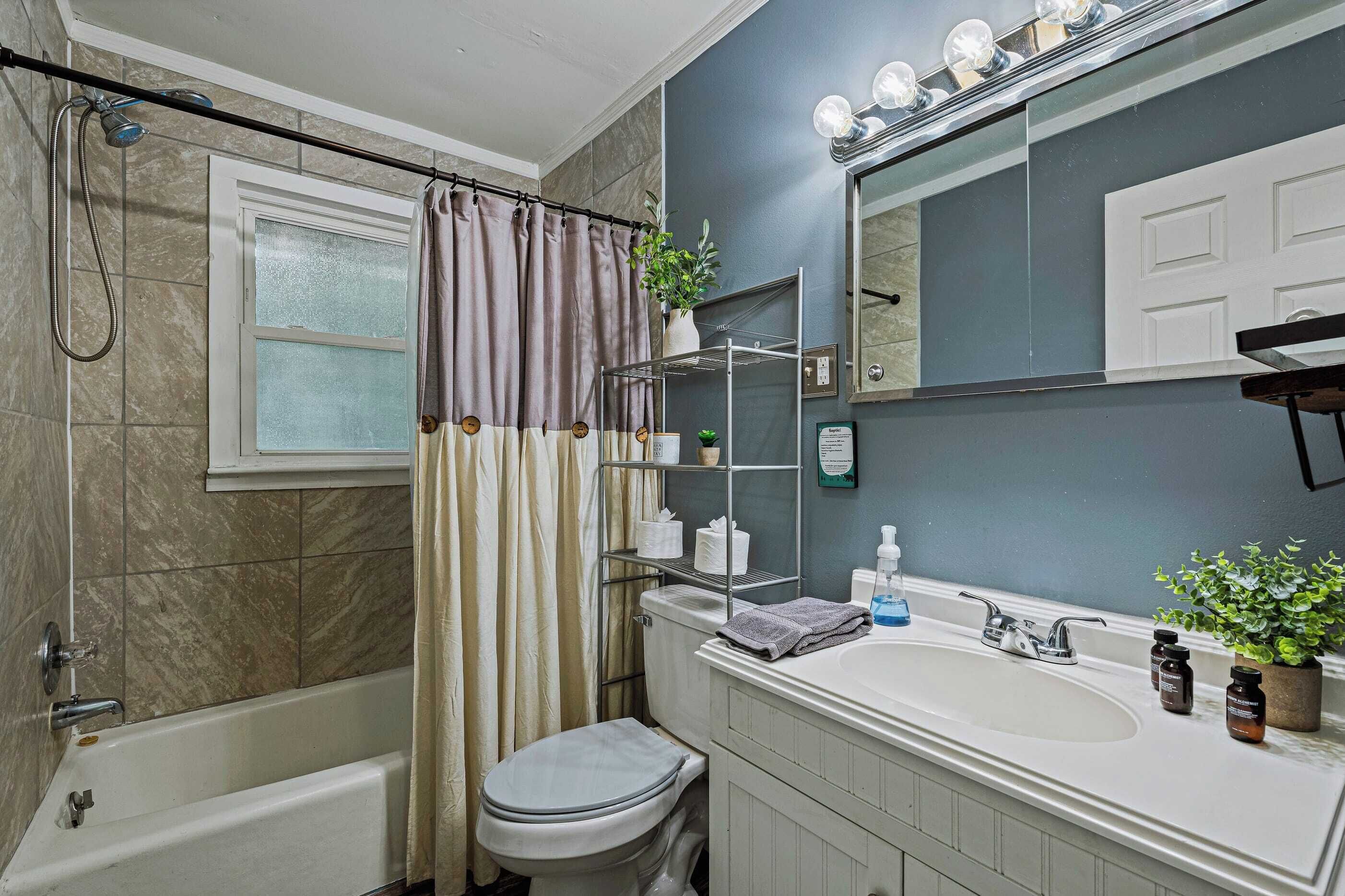 A bathroom with a bathtub, toilet, sink, and a mirror with lights.