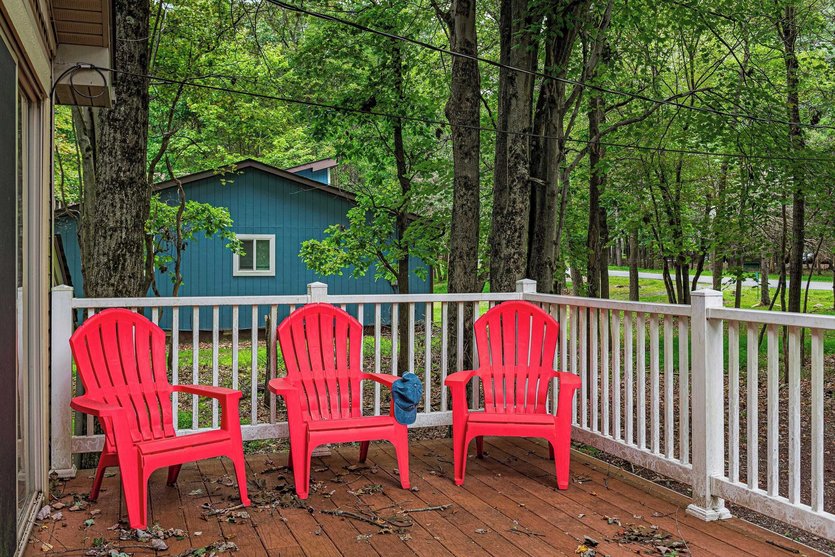 Une véranda avec trois chaises Adirondack rouges, une maison bleue en arrière-plan et une clôture blanche.