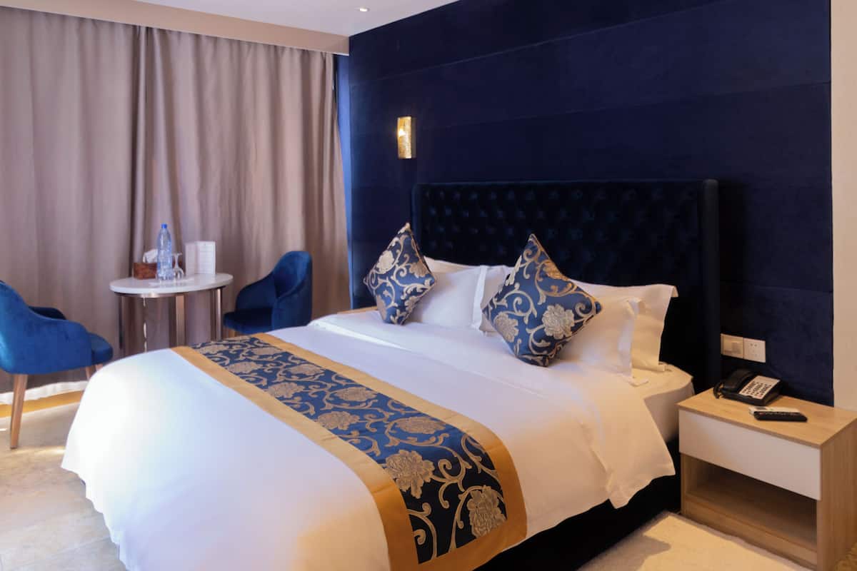 A hotel room with a large bed, a bedside table with a phone, a chair, and a small table with a water bottle.