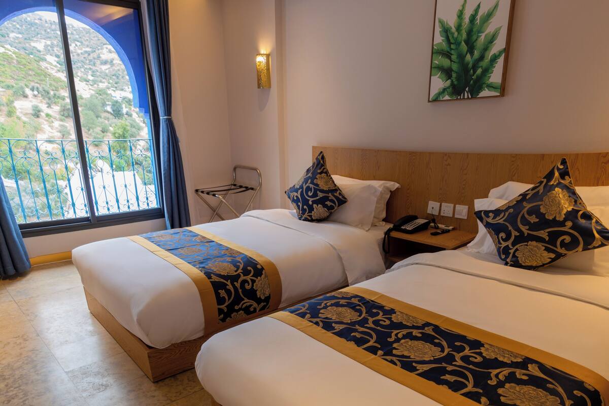 A hotel room with two beds, a view of the outdoors, a wall-mounted plant, and a telephone on the nightstand.