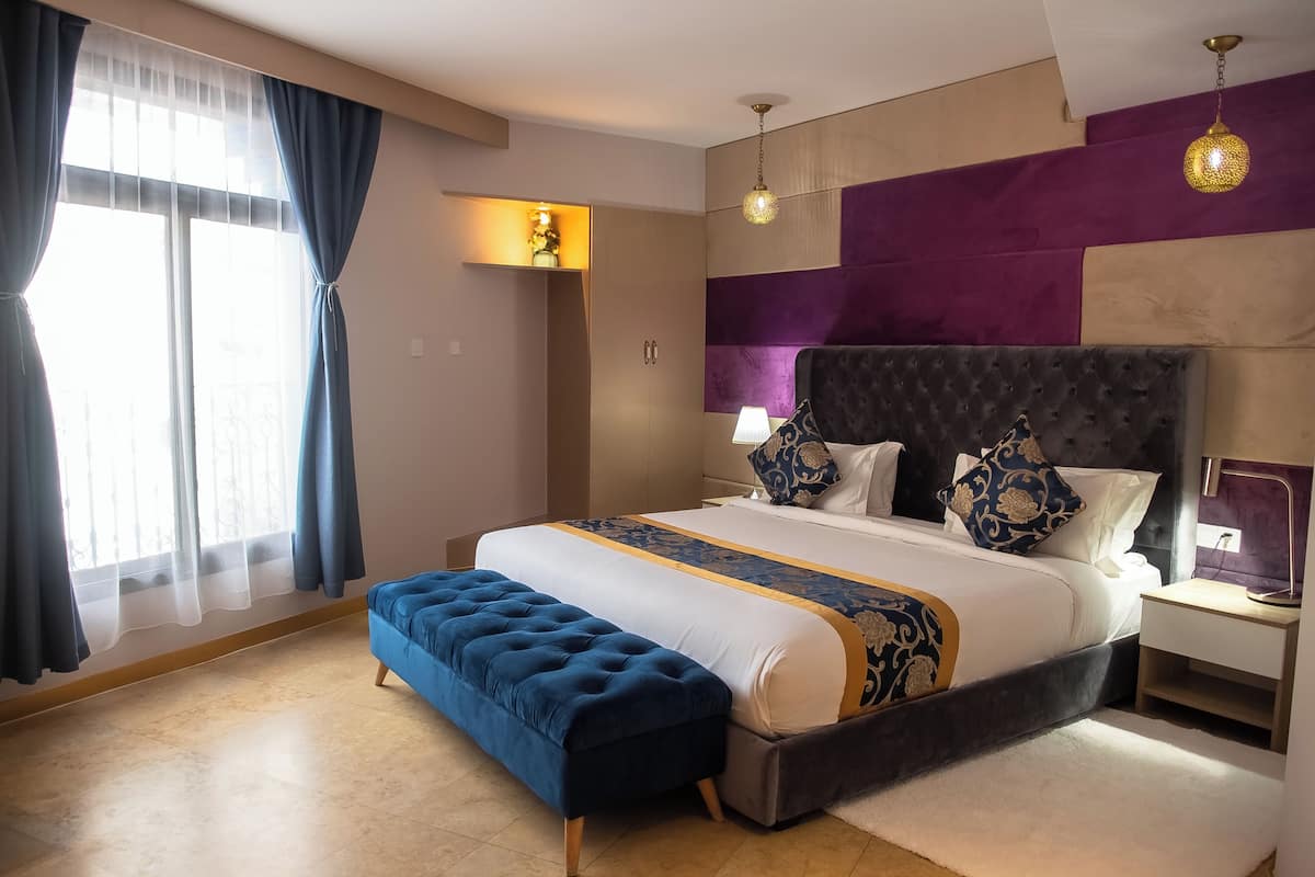 A modern hotel room with a large bed, a bench, a nightstand, and a lamp.