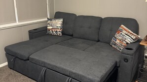 Ein graues Schlafsofa mit Stauraumschubladen, eine Wanddekoration mit Fischen und ein kleiner Tisch mit einer Lampe.