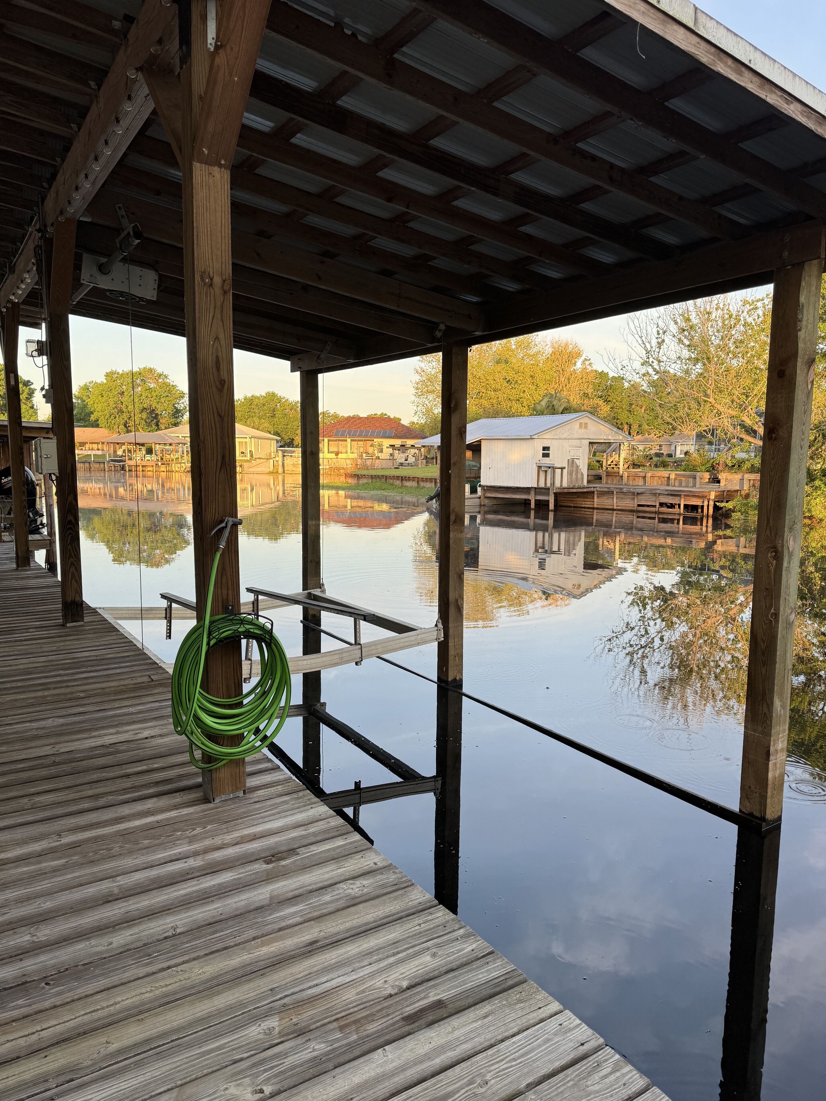 A wooden dock extending over a calm body of water, with a green hose coiled on the dock.