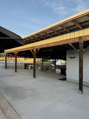 An outdoor covered area with a concrete floor, wooden beams, and metal roofing.