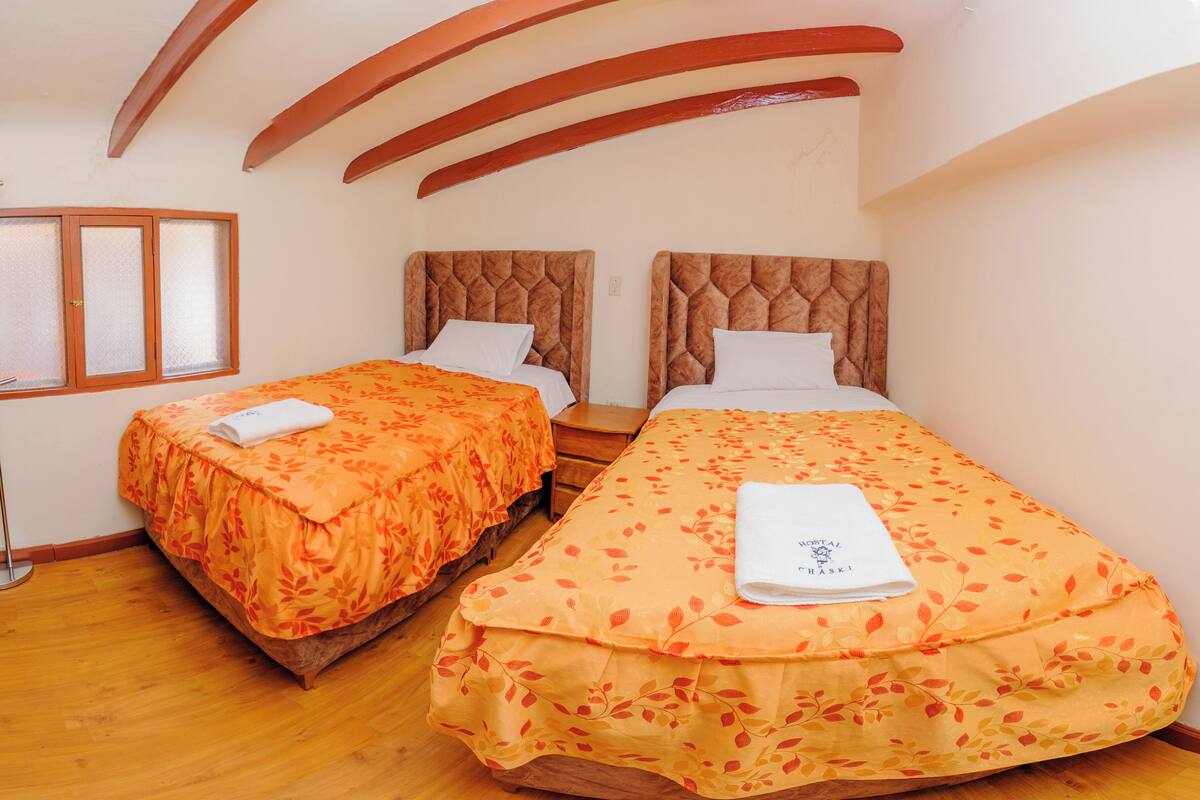 A room with two beds, each with a floral bedspread and white pillows, wooden headboards, and a wooden floor.
