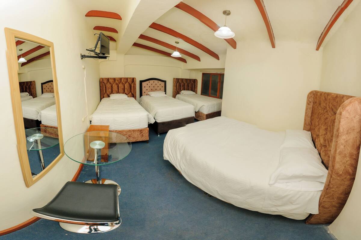 A hotel room with four beds, a glass table, a chair, and a mirror.