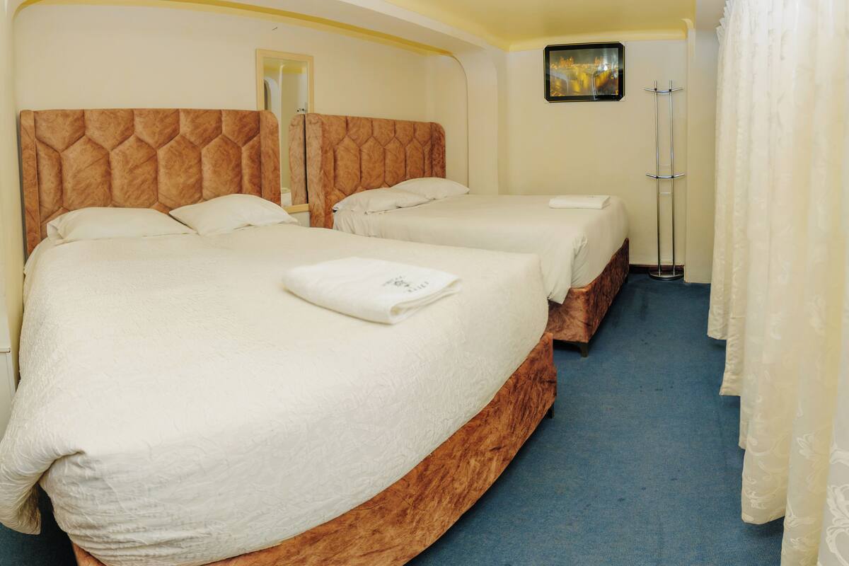 A hotel room with two beds, a mirror, a picture on the wall, and a floor lamp.