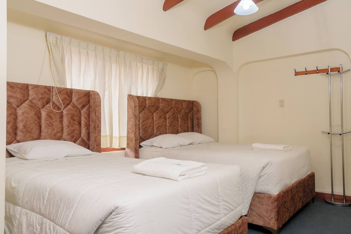 Two beds with headboards, a coat rack, and a window with curtains.