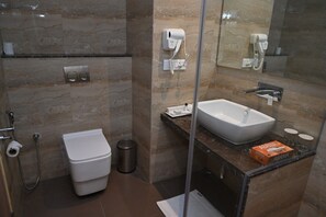 A modern bathroom with a glass-enclosed shower, a white toilet, a sink with a marble countertop, and a mirror. - Hotel The Ventus - A boutique Hotel  (New Delhi)