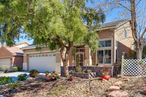 A two-story house with a garage, surrounded by a landscaped garden with various plants and a tree. - Live, Work. Play & Relax | Scenic SW Vegas. (Las Vegas)