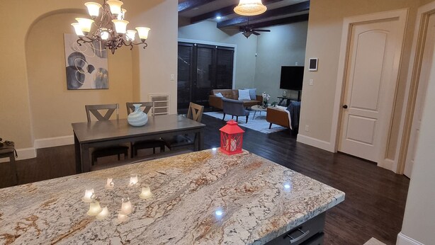 A spacious kitchen with a large marble island, dark cabinetry, and pendant lighting.