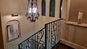 A staircase with ornate black railings, a chandelier, and a small shelf with a vase of flowers.