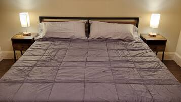 A bed with a gray quilt, two bedside tables with lamps, and a painting of a tree on the wall.