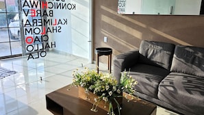 A modern living room with a large window, a sofa, a coffee table with flowers, and a small side table. - A03 SUPER CITY SUITE AT PLAZA ACEQUIA  (Cuautitlan Izcalli)
