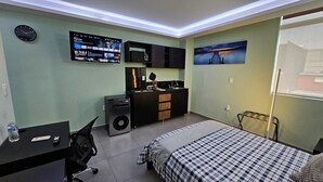 A bedroom with a bed, desk, chair, and a TV mounted on the wall displaying a program. - A03 SUPER CITY SUITE AT PLAZA ACEQUIA  (Cuautitlan Izcalli)