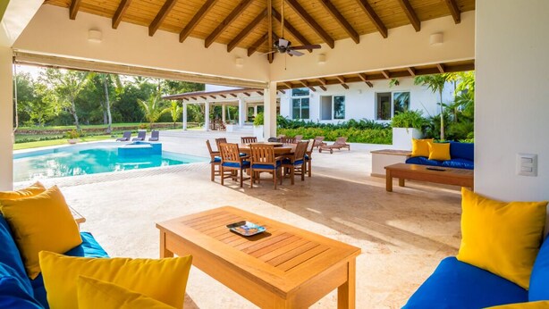 An outdoor covered patio with a pool, wooden furniture, and a view of the surrounding greenery. - Linksview Retreat, Casa de Campo (La Romana)