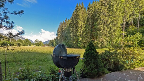 A portable grill on a stone patio with a forest and mountains in the background. - Stylish and cozy holiday home in Klais with terrace and garden, near MIttenwald. (Krün)