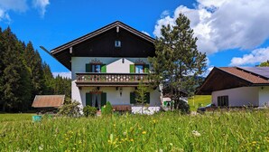 A two-story chalet with a balcony, surrounded by a lush meadow and pine trees. - Stylish and cozy holiday home in Klais with terrace and garden, near MIttenwald. (Krün)