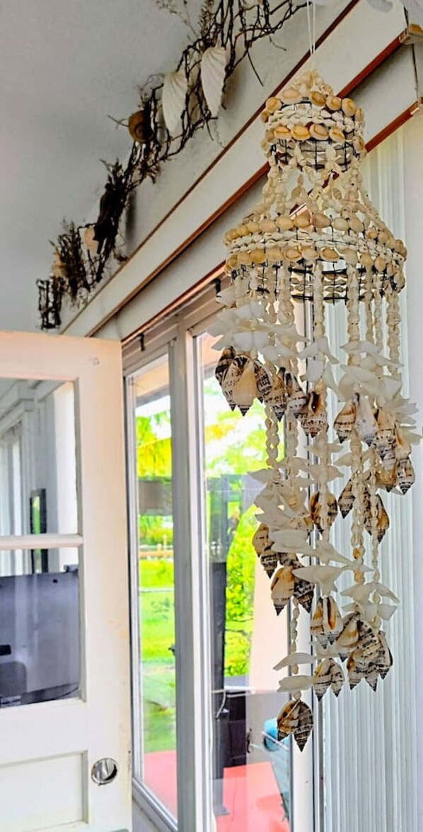 A room with a large window, a door, and a decorative hanging made of shells and beads.