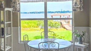 Comedor con una mesa redonda y sillas, ventilador de techo y vista a un jardín y una masa de agua.