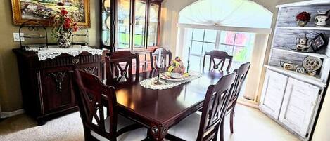 A dining room with a wooden table and chairs, a ceiling fan, a cabinet with glass doors, and a painting on the wall.