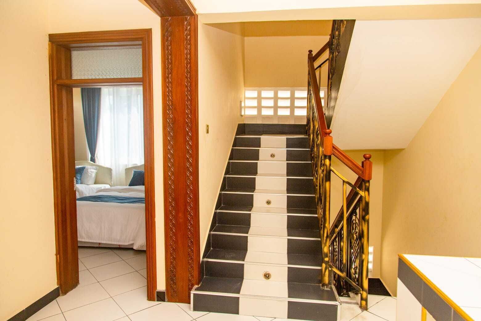 A staircase with black and white tiles, a wooden door frame, and a bed in the adjacent room.