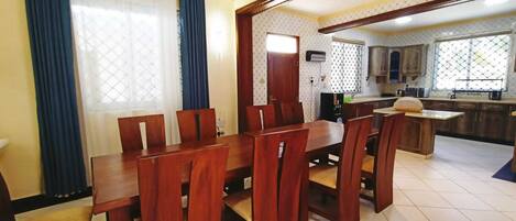 A dining area with a wooden table and chairs, a ceiling fan, and a kitchen in the background.