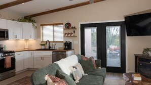 A modern kitchen with white cabinets, a microwave, and a stove. There is a green sofa with pillows and a coffee table with books and a remote control.