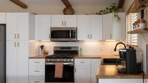 A modern kitchen with white cabinets, a stainless steel stove, a microwave, and a coffee maker.