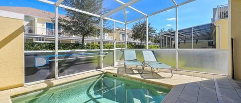 An indoor swimming pool with clear glass walls, a tiled floor, and a few lounge chairs.