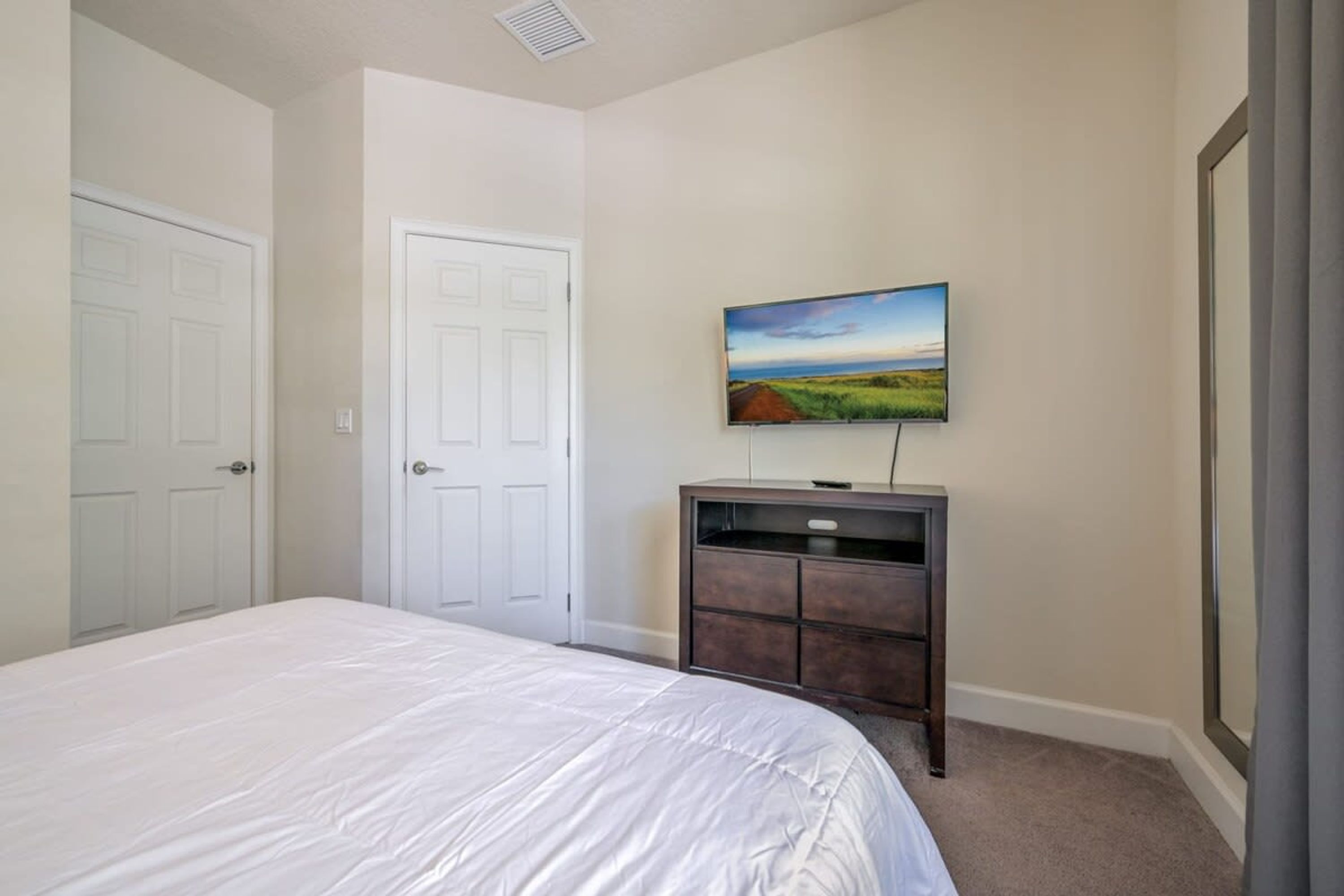 A bedroom with a bed, a dresser, a TV on the wall, and two doors.