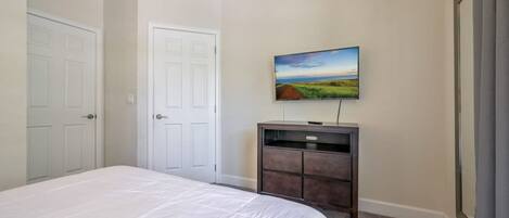 A bedroom with a bed, a dresser, a TV on the wall, and two doors.