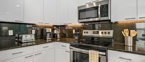 Una cocina moderna con armarios blancos, un microondas de acero inoxidable, una estufa y un tostador.