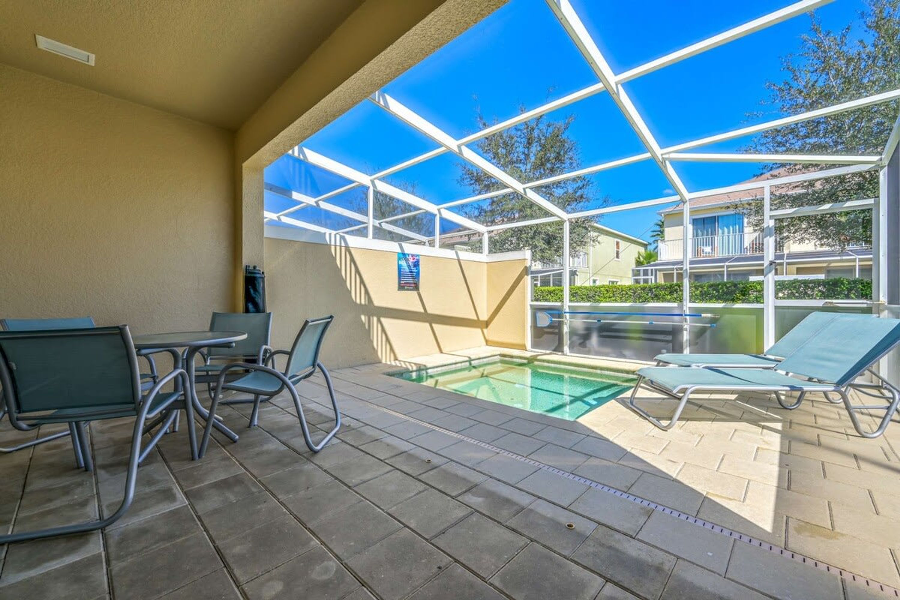 An outdoor pool area with lounge chairs and a table, surrounded by a glass enclosure.
