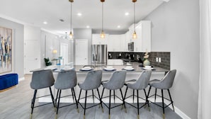 A modern kitchen with a central island, bar stools, pendant lighting, and a large refrigerator. - Luxury Incredible Themed Home Best Vacation (Kissimmee)