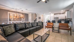 A modern living room with a sectional sofa, a coffee table, and a dining area with chairs. - Family Paradise Space Themed Perfect Location (Kissimmee)