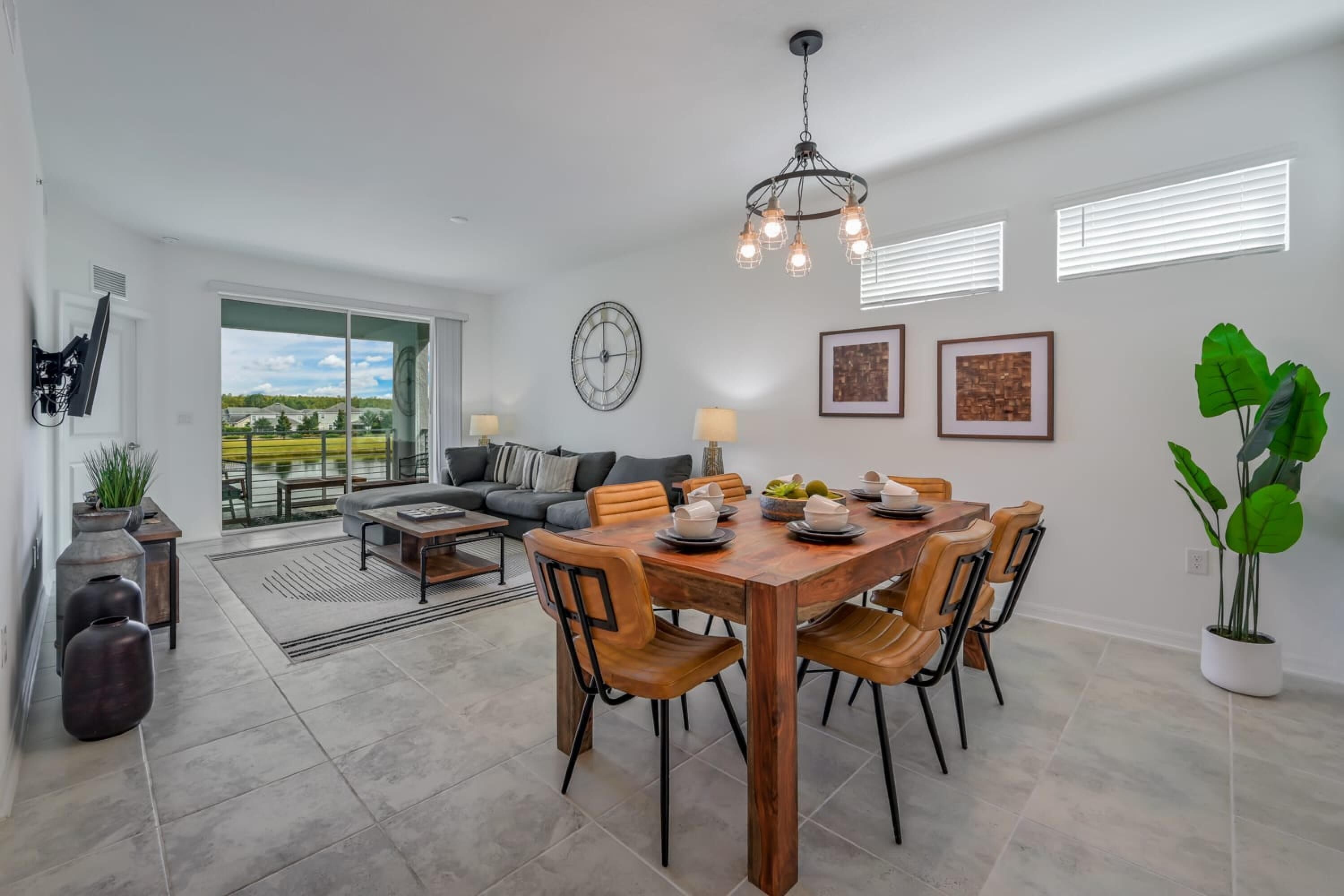 A spacious living area with a dining table, chairs, and a sofa. There is a large window providing a view of the outdoors.