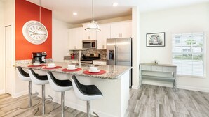 A modern kitchen with a central island, bar stools, a clock, and a dining area with a bench. - Cozy Home in Amazing Resort for Perfect Vacations (Davenport)