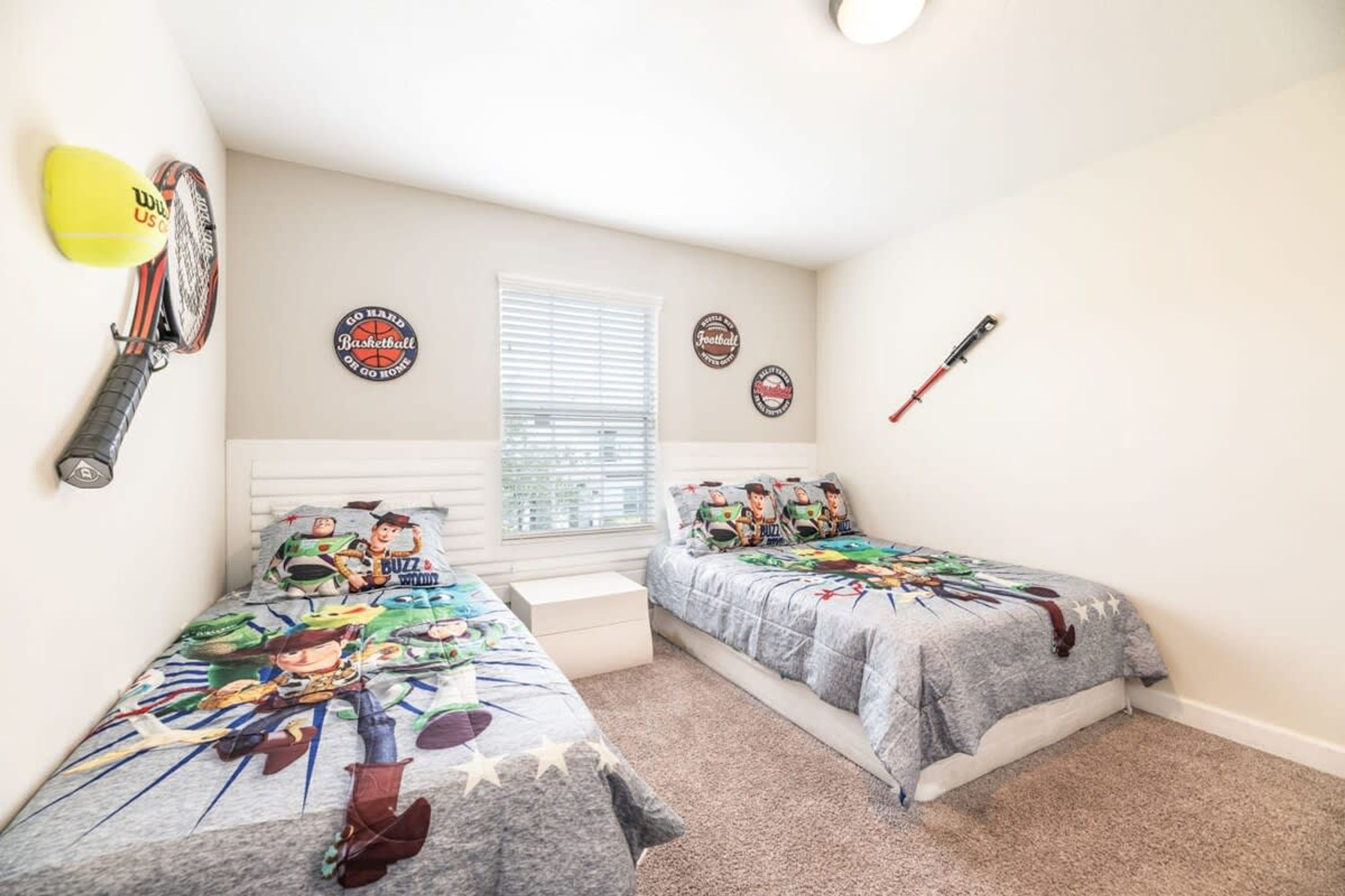 A bedroom with two beds, a window with blinds, and sports-themed wall decorations.