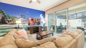 A living room with a large TV, a ceiling fan, and a view of the backyard through large glass doors.