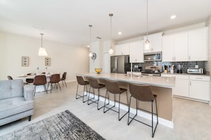 A modern kitchen with white cabinets, a central island with bar stools, and pendant lighting.