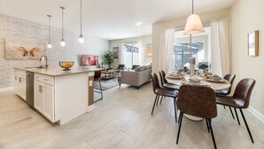 Une cuisine moderne dotée d’un îlot central, d’un coin repas avec des chaises et d’un salon avec un canapé.