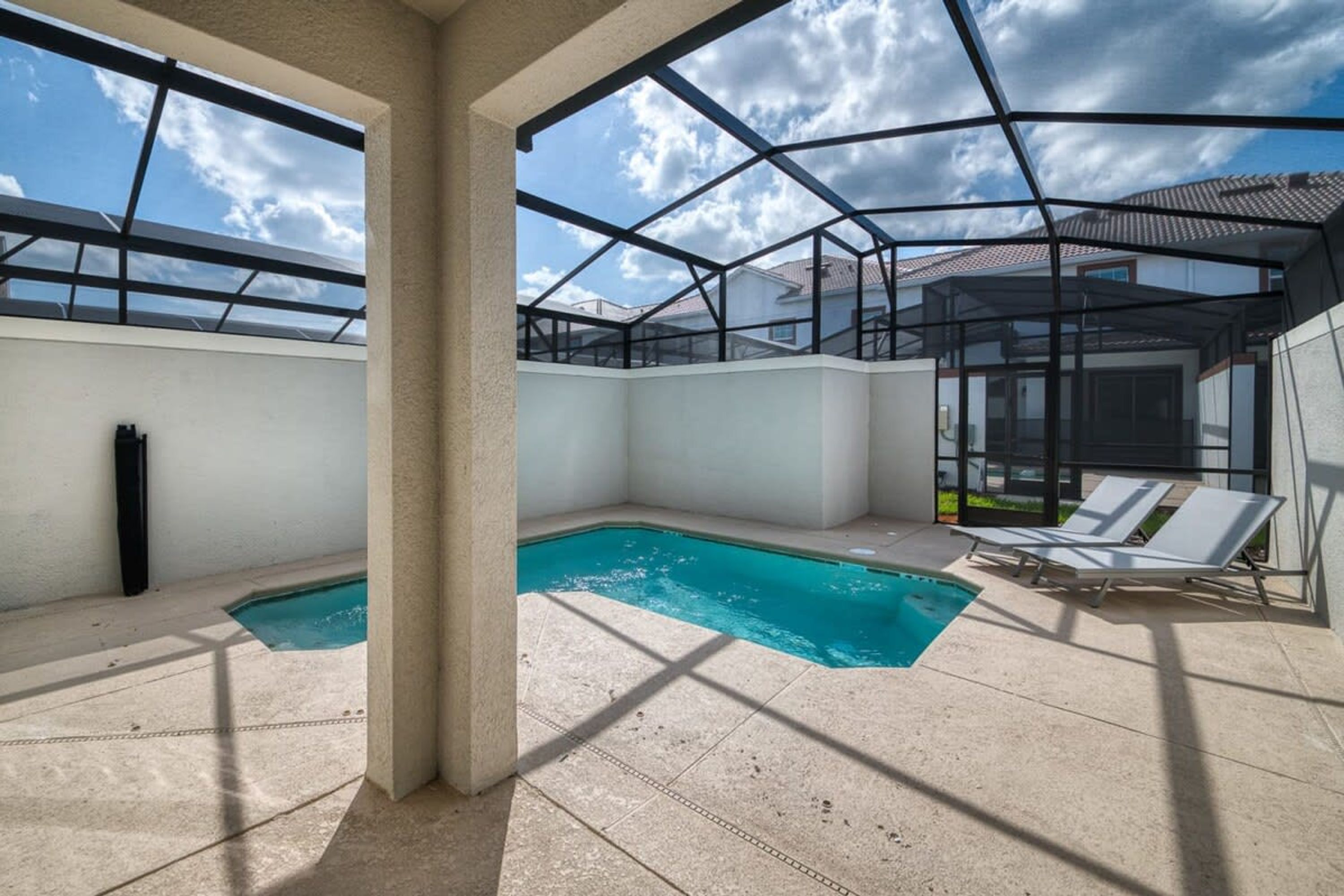 Zona de piscina al terrat amb una estructura de vidre, cel blau i vista dels edificis veïnals.