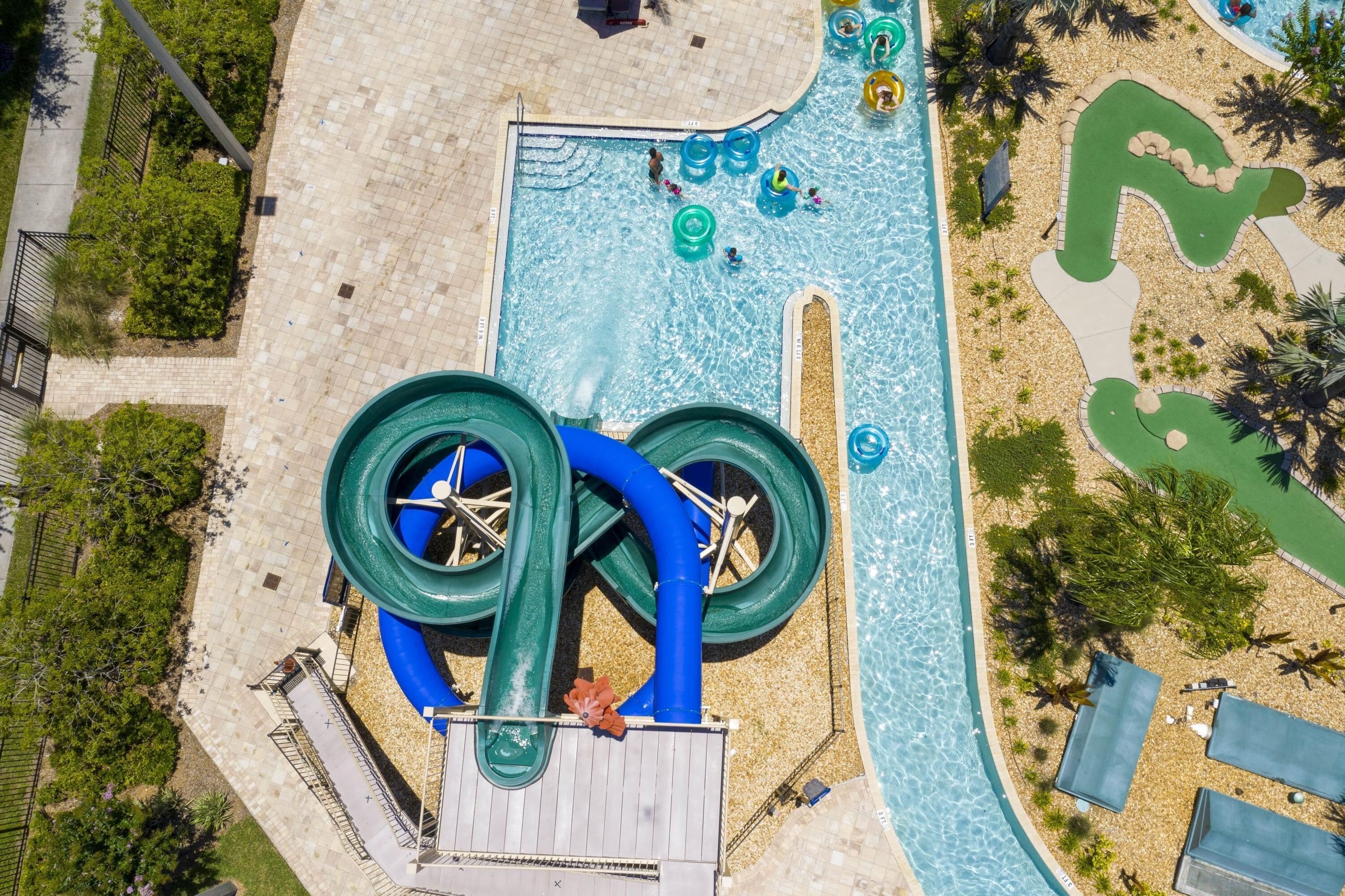 An aerial view of a water park with a large water slide, multiple water play areas, and surrounding landscaping.