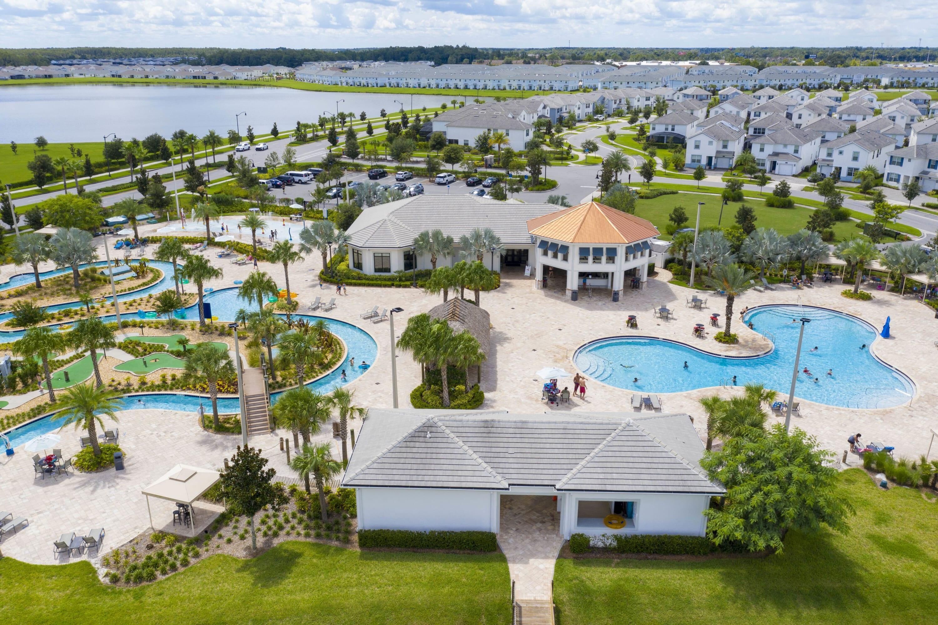 A resort with multiple swimming pools, a central building, and a lake in the background.