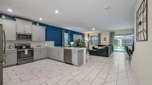 A modern kitchen with white cabinets, a central island, and a dining area with a gray sofa and table.