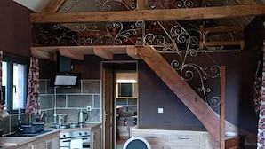 Una cocina amplia con una mesa de comedor de madera, una escalera con barandilla de hierro forjado y una araña.