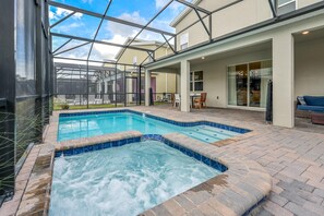 Une piscine avec un jacuzzi, entourée d’un patio couvert aménagé avec du mobilier d’extérieur.