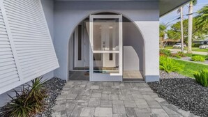 Una casa moderna con puerta de cristal, un camino de hormigón y un jardín ajardinado.