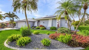 Una casa residencial con un jardín bien cuidado, que incluye diversas plantas y un camino de entrada.